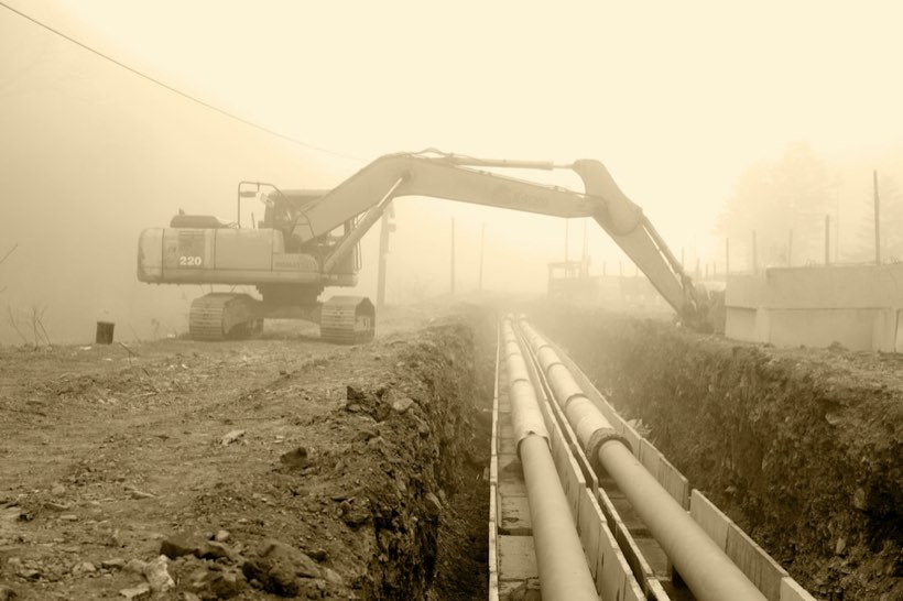An excavator laying large water pipes in a trench during pipeline works